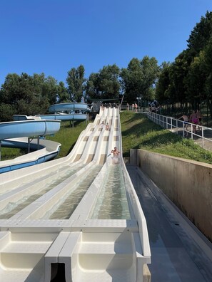 Eine Wasserrutsche mit mehreren Bahnen, umgeben von viel Grün und Bäumen.