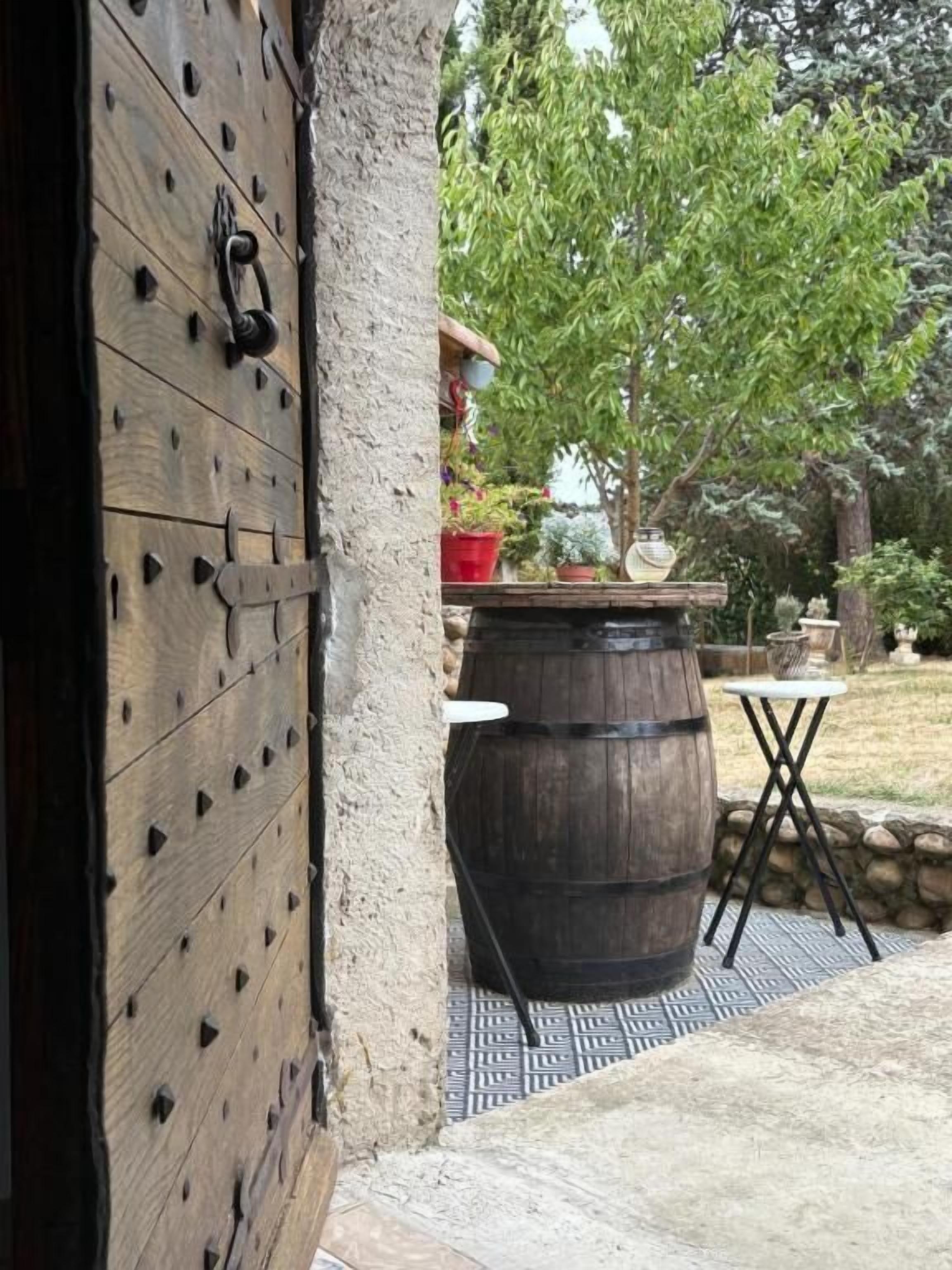 An open wooden door, a large barrel, a small table, and a stone wall.