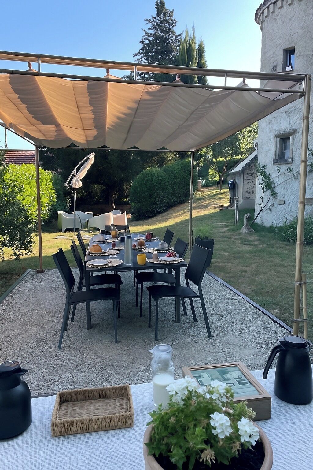 An outdoor dining area with a table set for four, surrounded by chairs, under a canopy.
