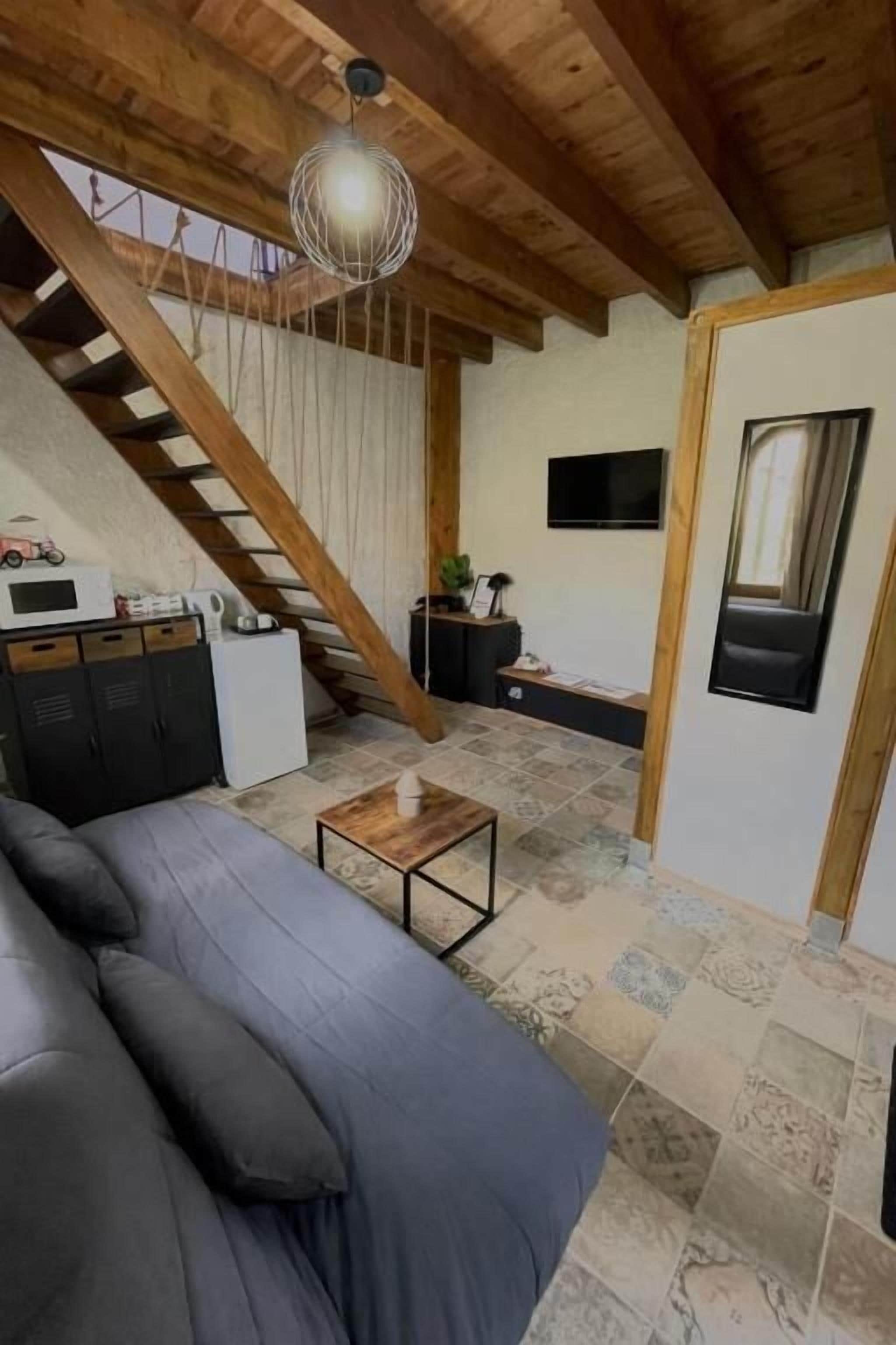 Una habitación con sofá, una mesa pequeña, una escalera, televisor y una puerta.