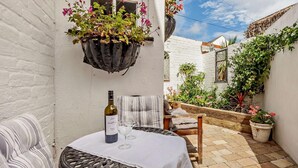 En terrasse med et bord, stole, en hængende blomsterkrukke og en flaske vin.