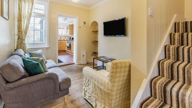 Ein Wohnzimmer mit einer Couch, einem Sessel und einem an der Wand befestigten Fernseher.