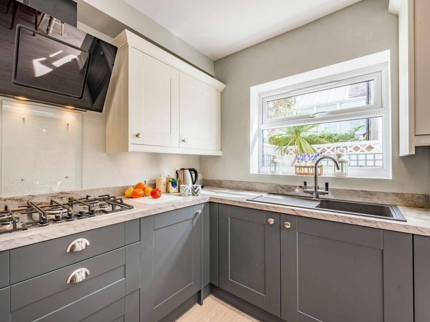 A modern kitchen with grey cabinets, a gas stove, a sink, and a window with a view of greenery.