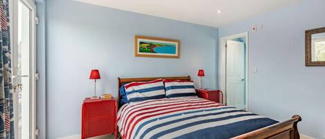 Une chambre à coucher avec un lit, deux tables de chevet, une fenêtre avec des rideaux et une porte.