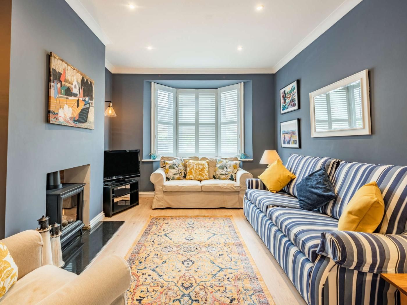 A living room with a sofa, a television, a fireplace, a rug, and a bay window with shutters.