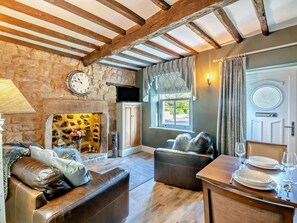Ein gemütliches Wohnzimmer mit Kamin aus Stein, Ledersofas, einem Esstisch und einer Wanduhr.