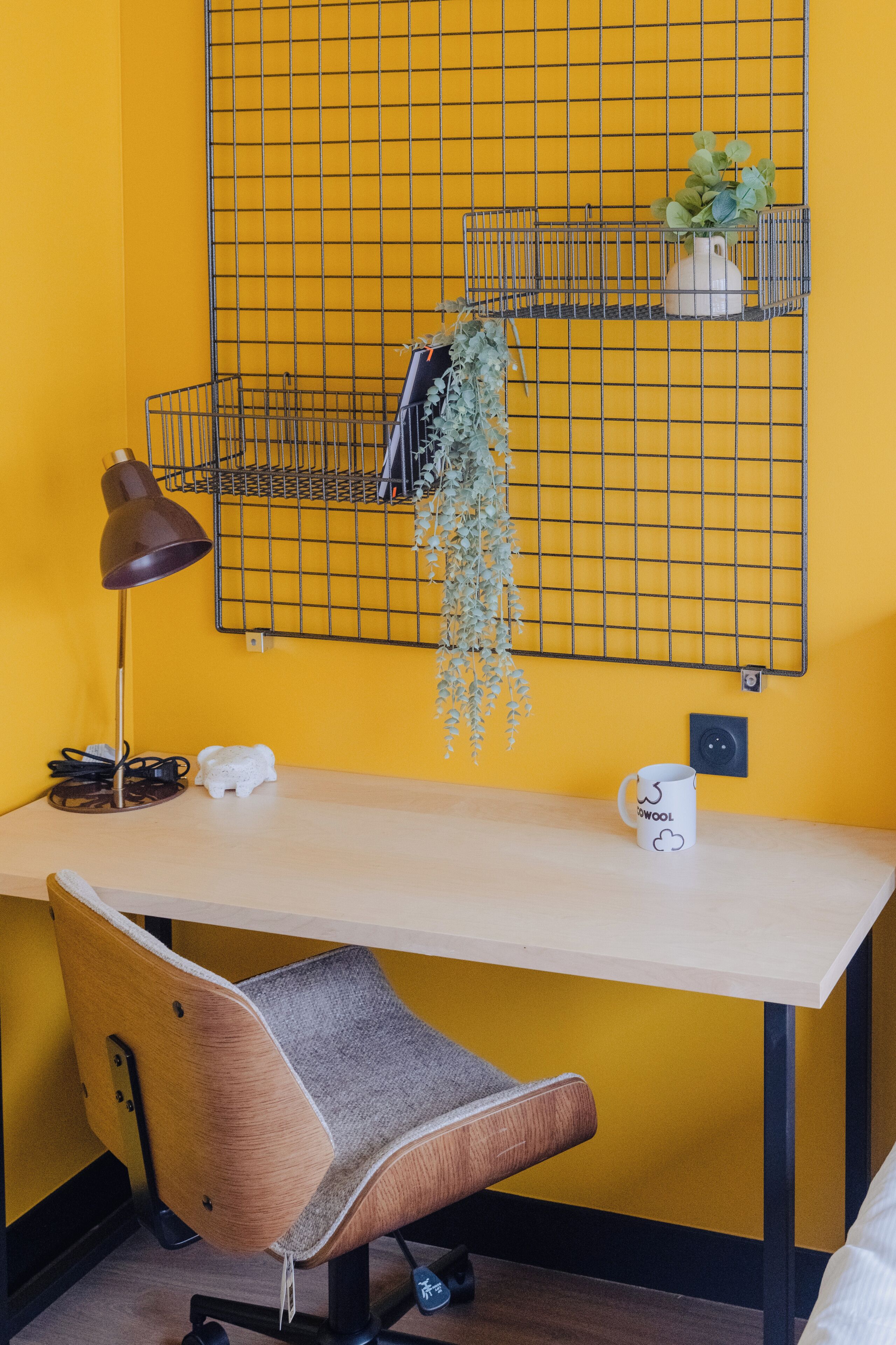 Un espacio de trabajo con escritorio, silla, lámpara y estante en la pared con plantas.