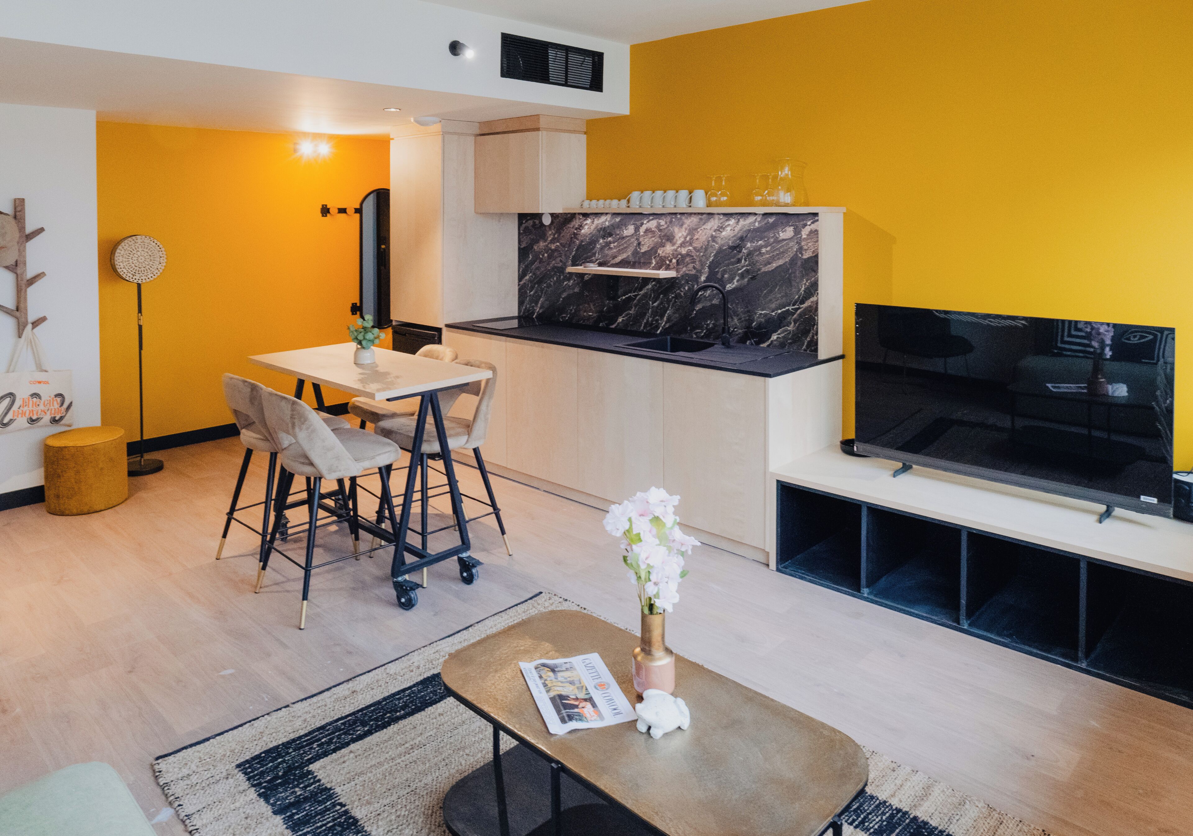 Una sala de estar moderna con comedor, cocina con cubierta negra y televisor de pantalla plana montado en la pared.