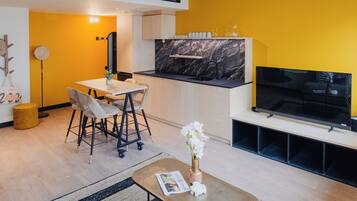 Una sala de estar moderna con comedor, cocina con cubierta negra y televisor de pantalla plana montado en la pared.