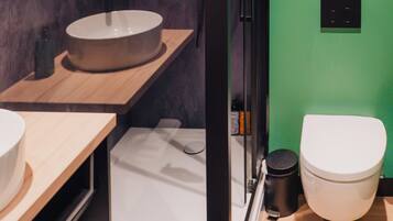 A modern bathroom with a round sink, a toilet, and a shower area.