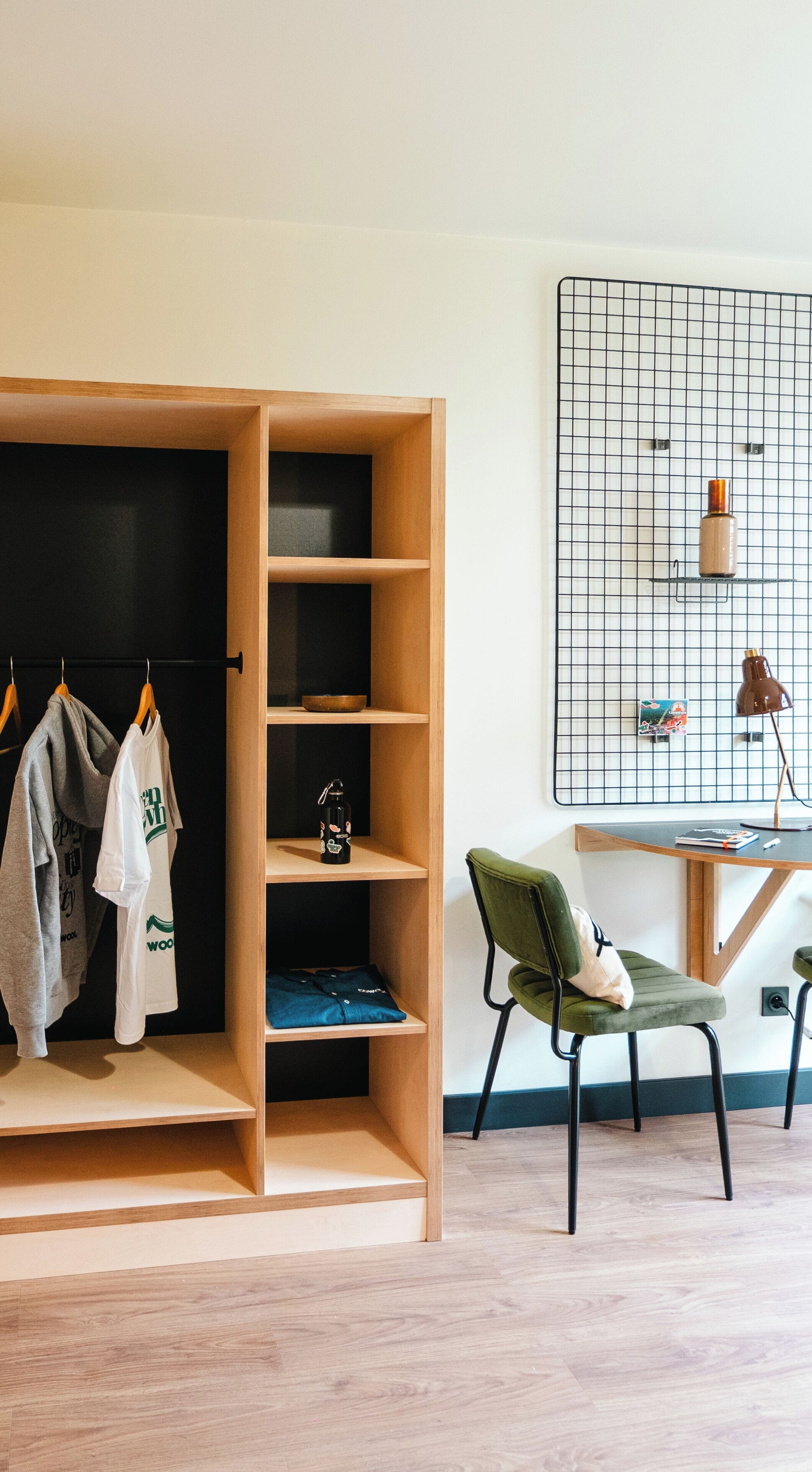 Una habitación con un armario de madera, una silla verde, un escritorio con una lámpara y un patrón de cuadrícula en la pared.
