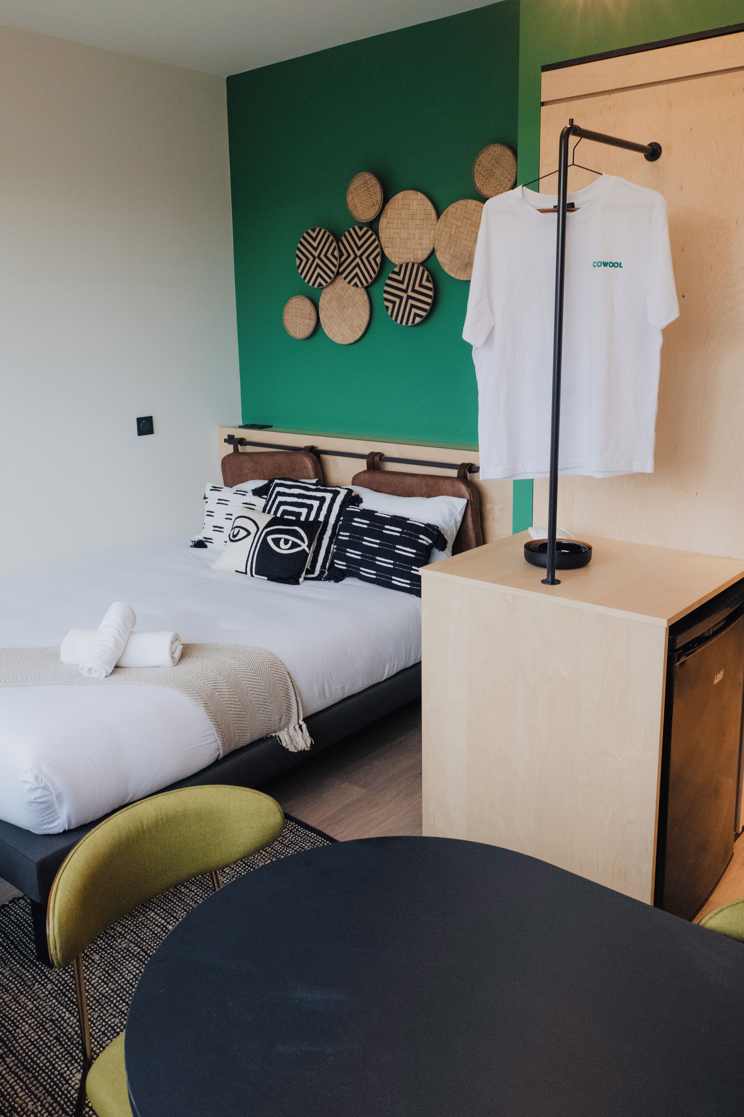 A modern hotel room with a bed, a bedside table, a chair, a wardrobe, and a wall with decorative plates.
