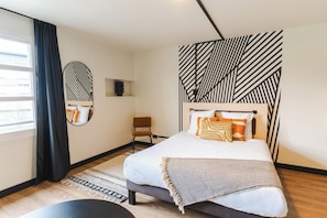 A modern bedroom with a large bed, a side table, a chair, a mirror, and a geometric-patterned headboard. - Cowool Créteil (Créteil)