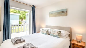 Ett hotellrum med en stor säng, utsikt över omgivningarna, en tavla på väggen och en sänglampa.