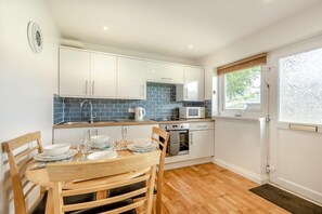 A modern kitchen with white cabinets, a blue-tiled backsplash, a microwave, and an oven. - 2 Bed in Brixham (oc-bx081) (Brixham)