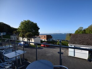 A balcony with outdoor seating, a view of the sea, and a parking area with cars. - 2 Bed in Brixham (oc-bx081) (Brixham)