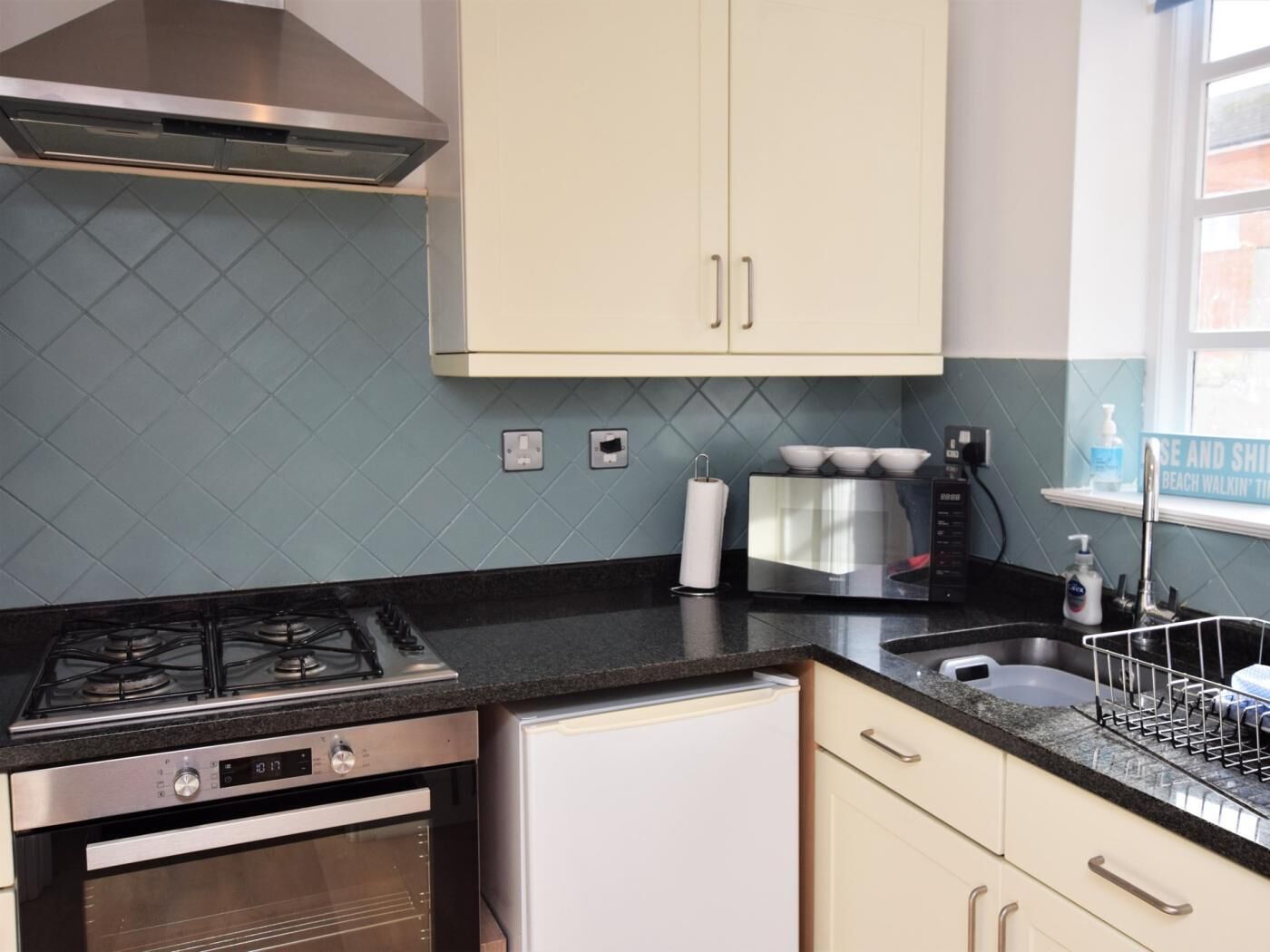 A kitchen with a gas stove, oven, microwave, and a sink with a dish rack.