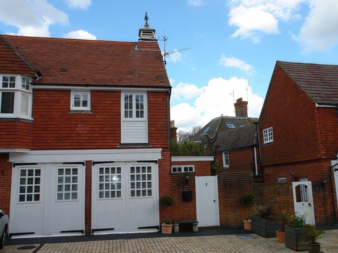 A two-story brick house with a garage, a white door, and a small garden area with potted plants.