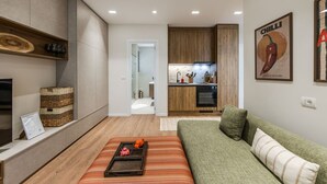A modern living room with a sofa, a wooden shelf, and a kitchen in the background. - Kiti Apartment Beach Escape (Vlorë)