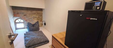 Una habitación pequeña con una cama, un aparador de madera y un refrigerador negro con pantalla digital.