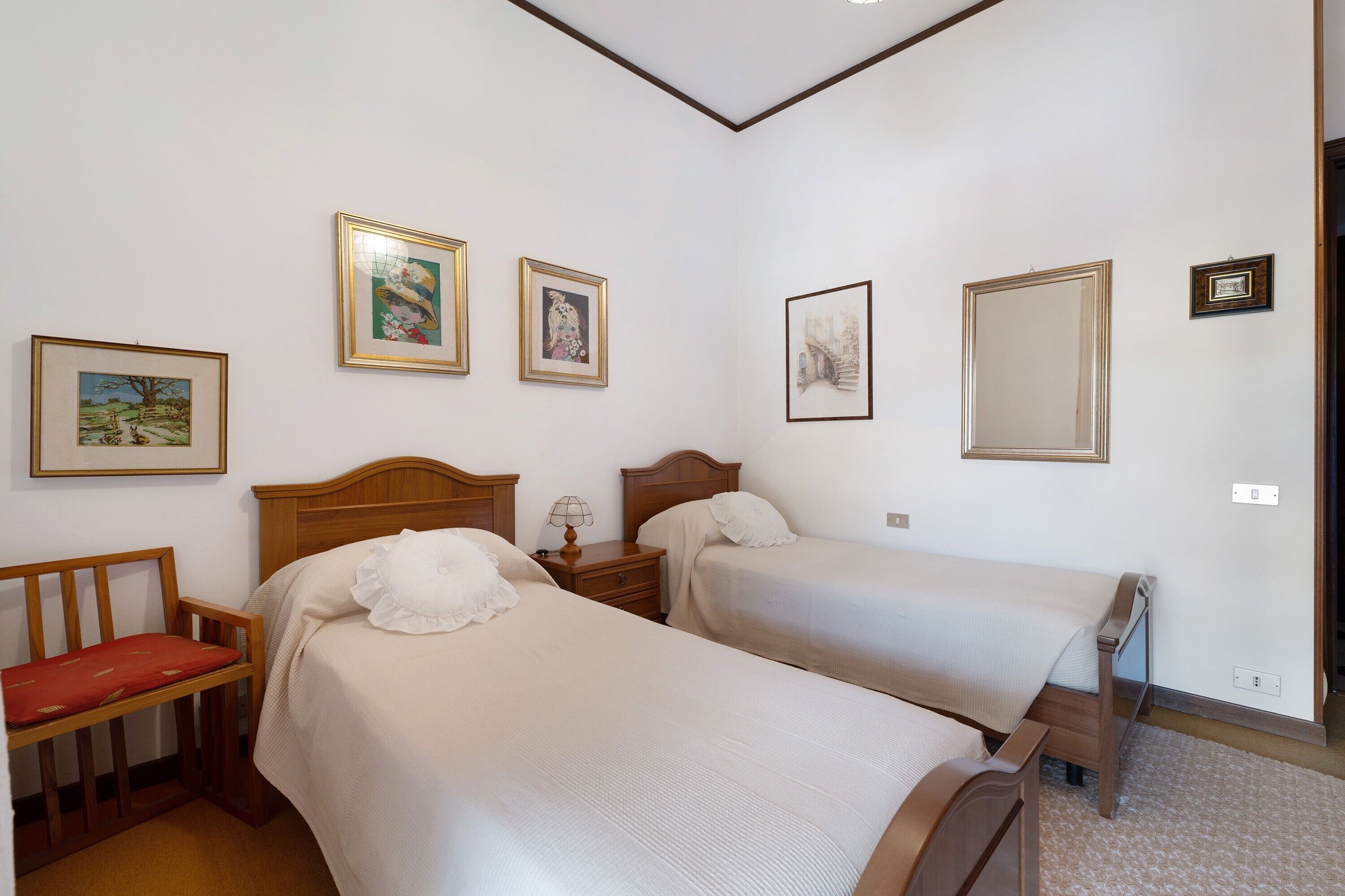 A bedroom with two beds, a wooden nightstand, a lamp, and framed pictures on the wall.