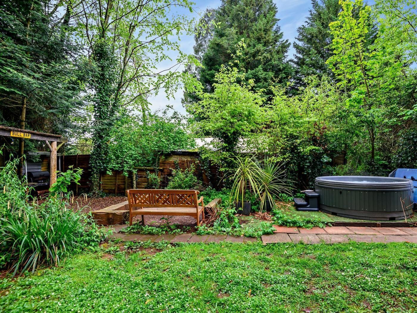 A garden with a wooden bench, a hot tub, and a grill area.