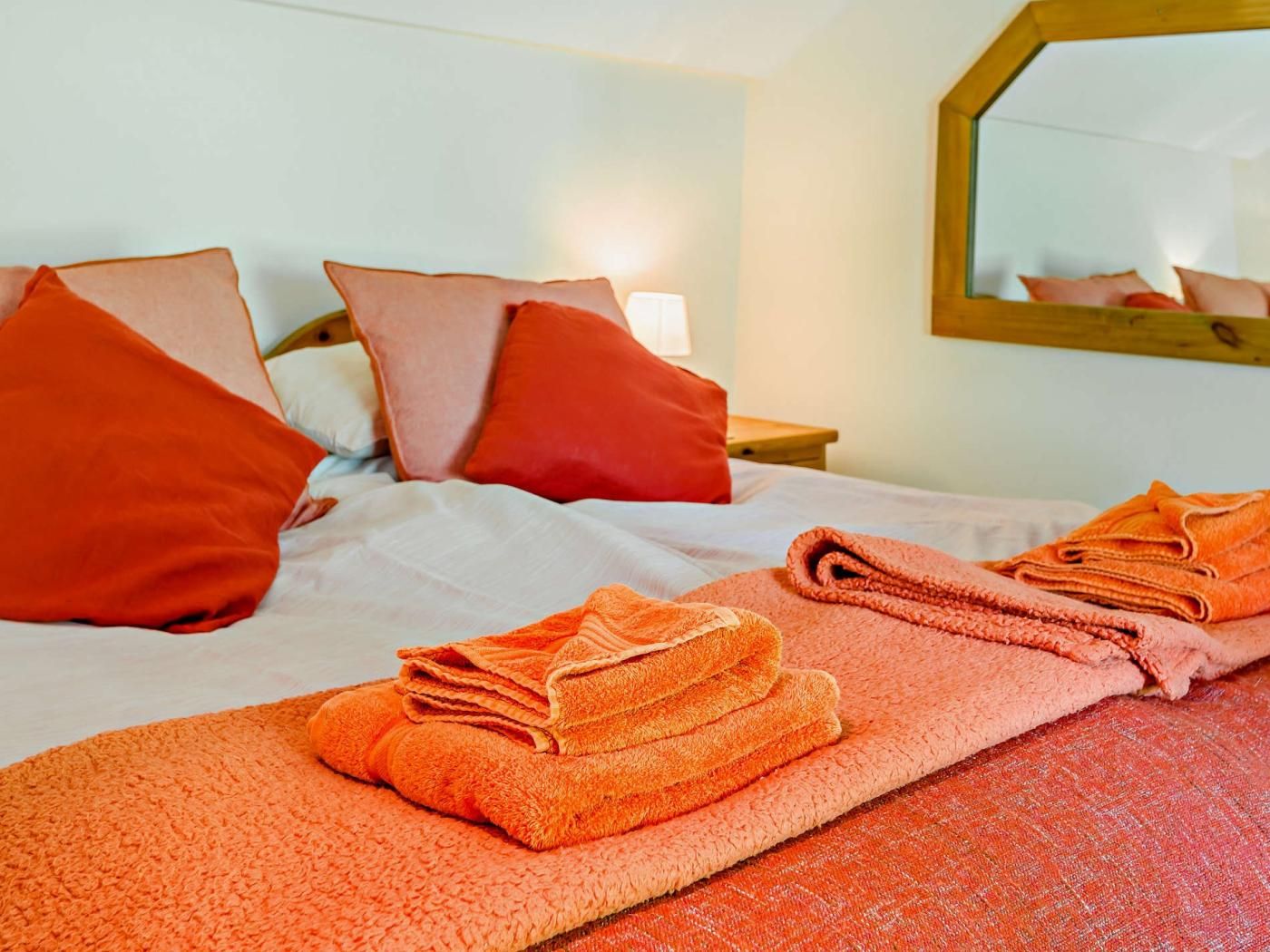 Een hotelkamer met een bed, kussens, een opgevouwen oranje handdoek en een spiegel aan de muur.