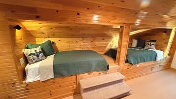 Interno di una cabina con due letti a castello in legno, una piccola panca e soffitto in legno.