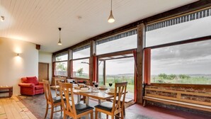 Un vaste espace de salle à manger avec des chaises et des tables en bois, de grandes fenêtres offrant une belle vue et un canapé rouge.