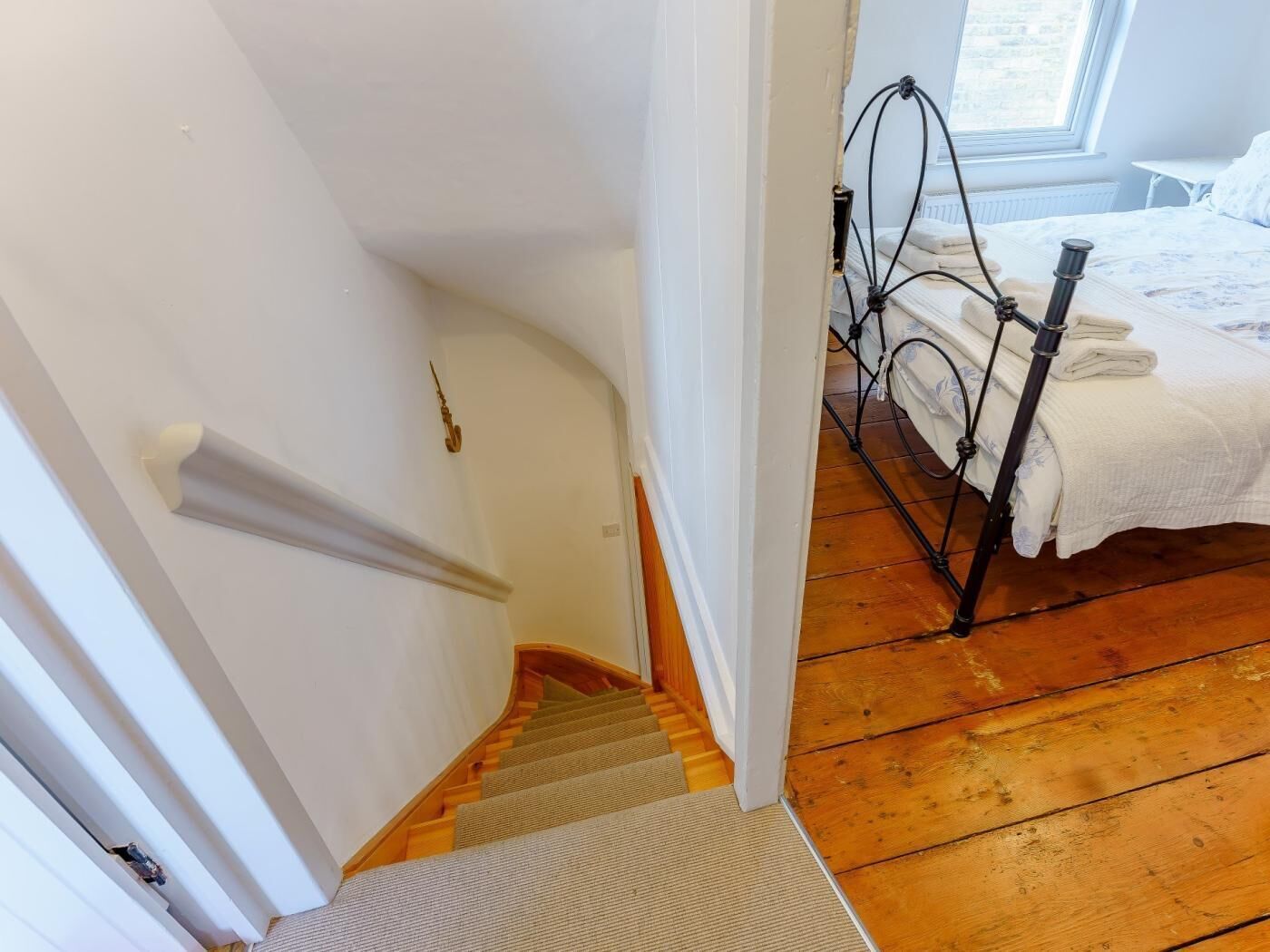 A staircase leading to a bedroom with a bed, a window, and a door.