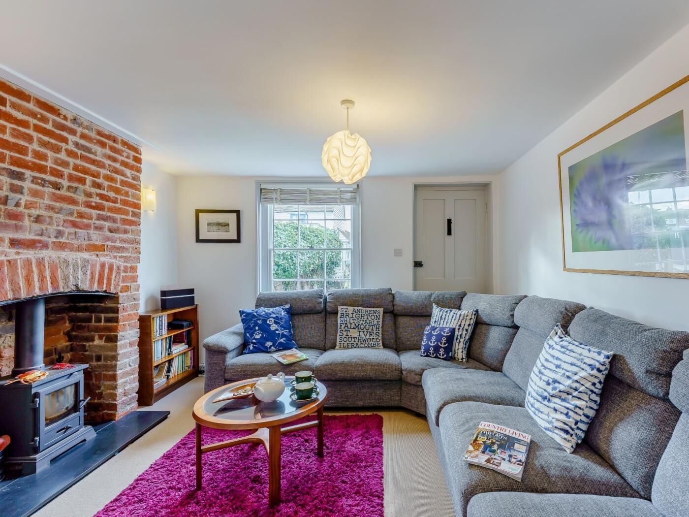 A living room with a brick fireplace, a grey sofa, a coffee table, and a bookshelf.