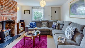 A living room with a brick fireplace, a grey sofa, a coffee table, and a bookshelf. - 3 Bed in Whitstable (oc-wcc12) (Whitstable)