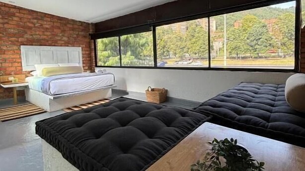 Una habitación moderna con un gran ventanal, una cama, un sofá y una mesa de madera con una planta.