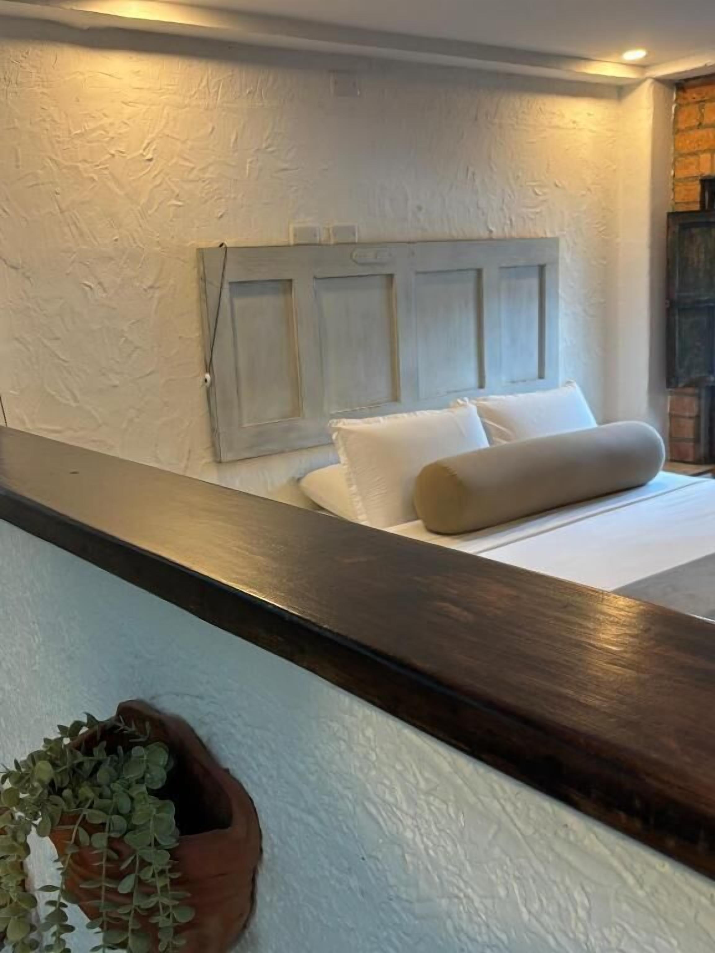A bedroom with a bed, a headboard, a dark wooden bench, and a potted plant.