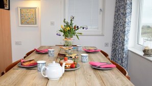 Una mesa de madera con una tetera blanca, servilletas rosas y un centro de mesa floral.