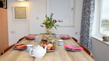 A wooden dining table with a white teapot, pink napkins, and a floral centerpiece.