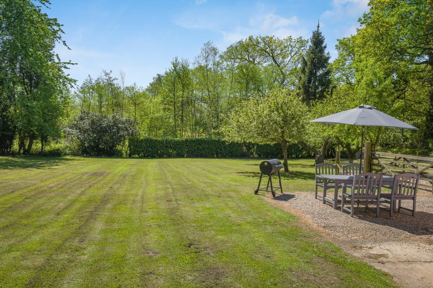 A well-maintained lawn with a barbecue grill, outdoor seating, and a hedge in the background.