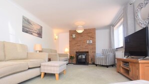 A living room with a sofa, ottoman, fireplace, television, and a decorative mirror. - 3 Bed in Dereham (oc-56661) (Horningtoft)