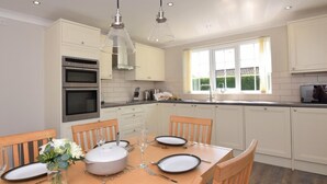 A modern kitchen with white cabinets, a double oven, and a dining area set for four with a table, chairs, and a vase of flowers. - 3 Bed in Dereham (oc-56661) (Horningtoft)
