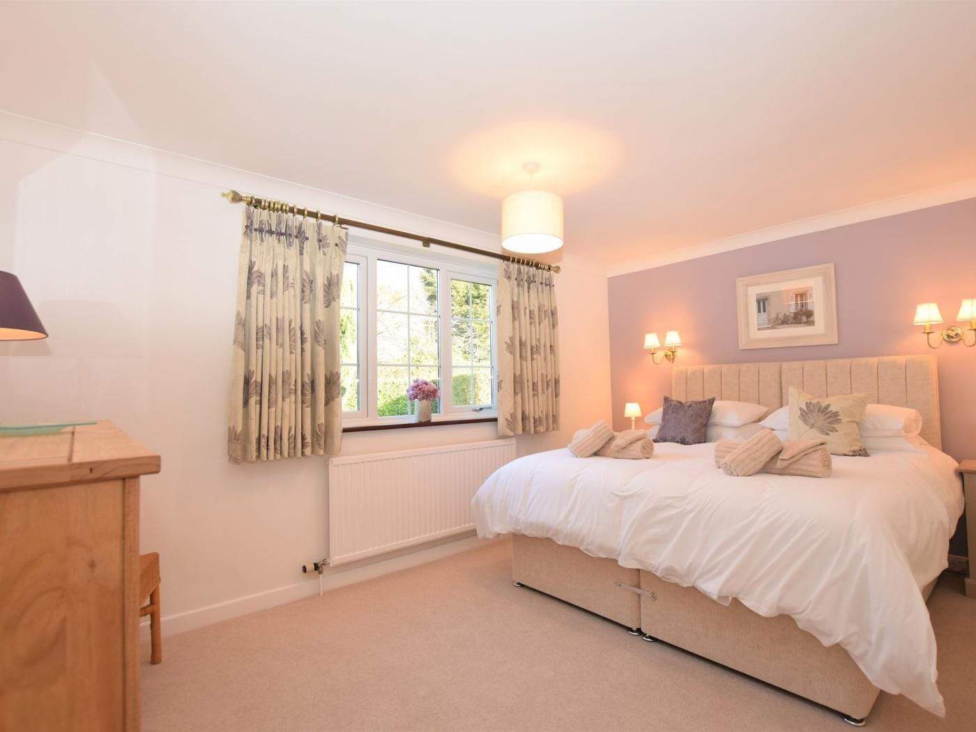 A bedroom with a bed, a window with curtains, a bedside table, and wall-mounted lights.