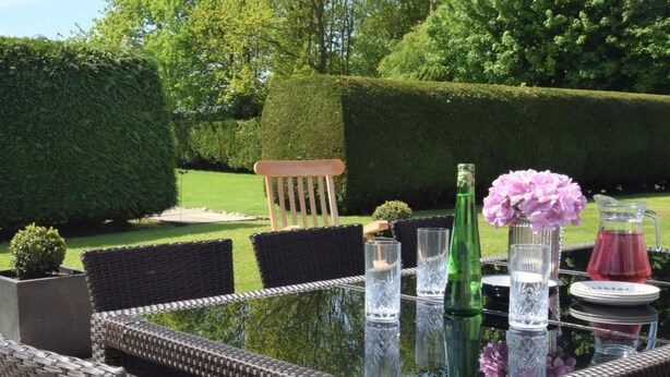 A glass-top table with wicker chairs, a bottle, glasses, and a pitcher in a garden setting. - 3 Bed in Dereham (oc-56661) (Horningtoft)