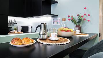 A kitchen counter with croissants, a coffee pot, a fruit bowl, and a vase with flowers.