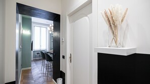 Een gang die uitkomt in een eetruimte, met een raam, een deur met een decoratieve knop en een vaas met pampa gras op een plank.