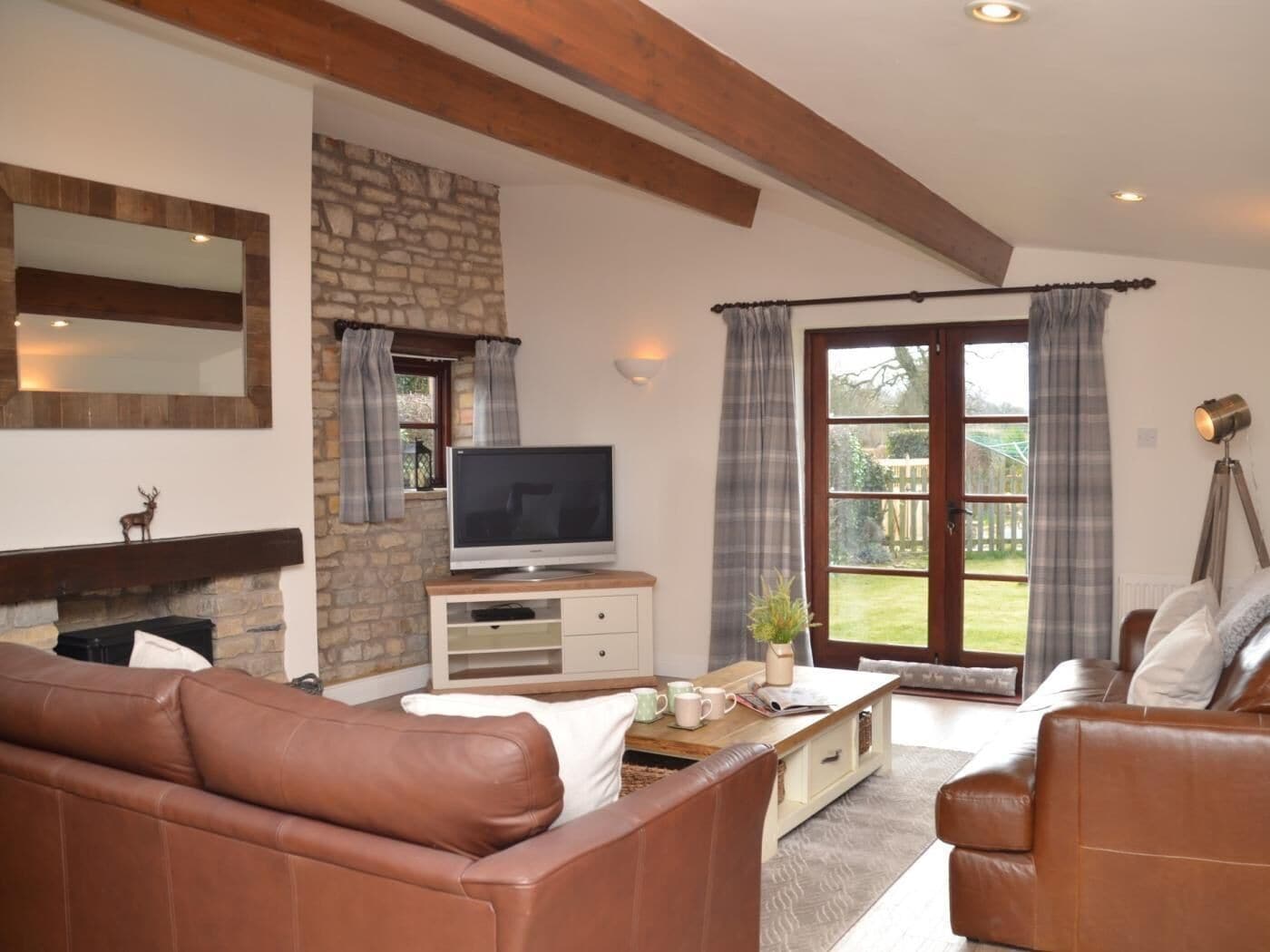 A living room with leather sofas, a stone fireplace, a television, and a large window with curtains.