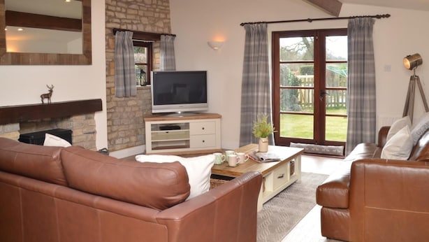 Ein Wohnzimmer mit Ledersofas, einem Steinkamin, einem Fernseher und einem großen Fenster mit Vorhängen.