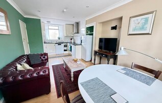 Un espacio habitable compacto con comedor, sofá, televisión y cocina al fondo.