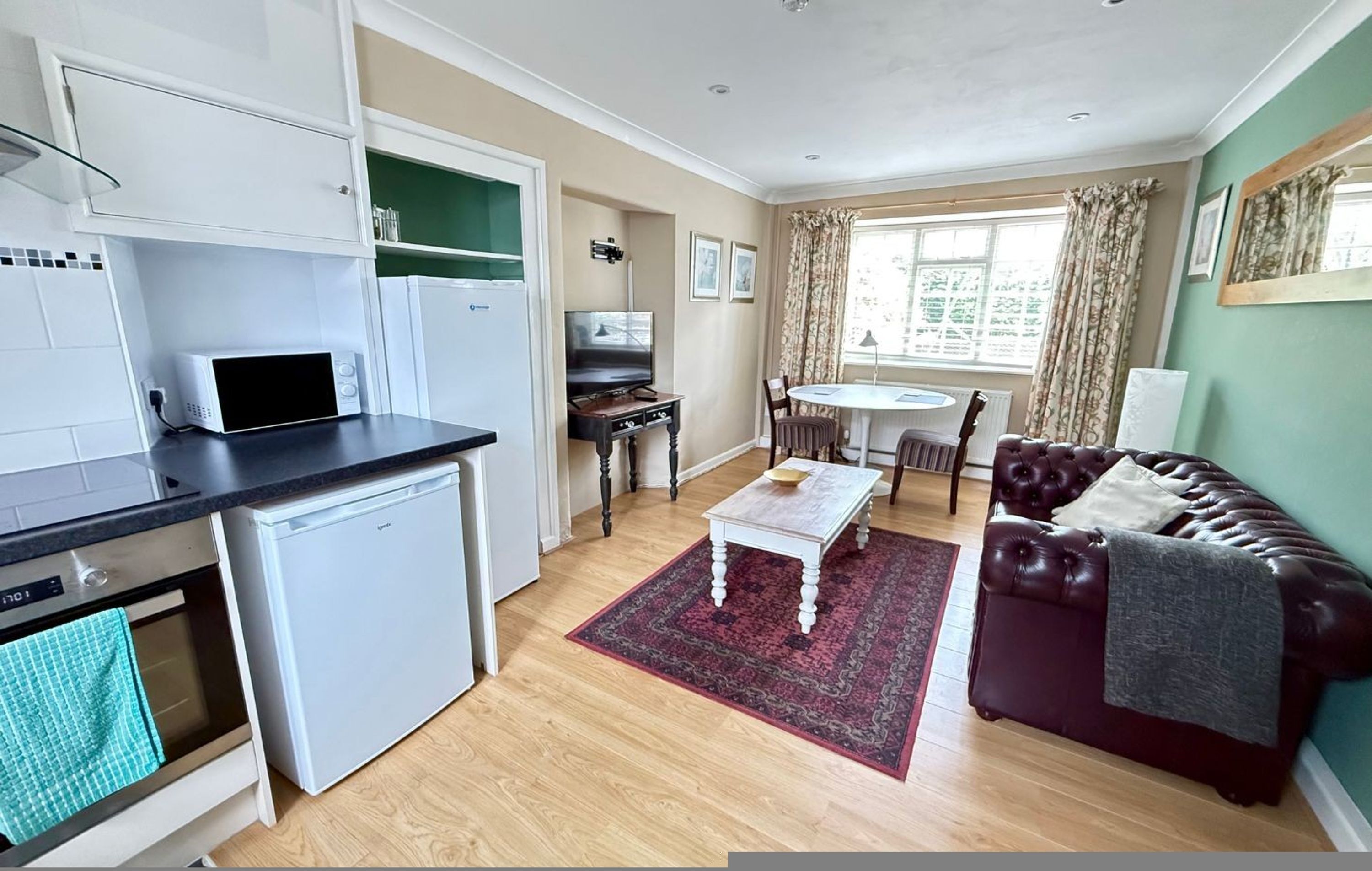 Un espacio habitable compacto con kitchenette, una zona de comedor con mesa y sillas, y una sala de estar con sofá.