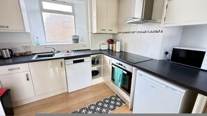 A modern kitchen with white cabinetry, a black countertop, a window, and a microwave. - Alway at Lifton Hall (Lifton)