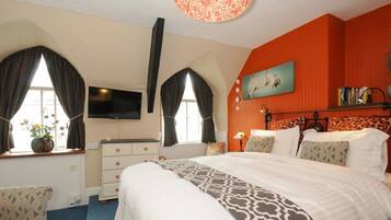 A hotel room with a large bed, a television, a desk with a chair, and a window with curtains.