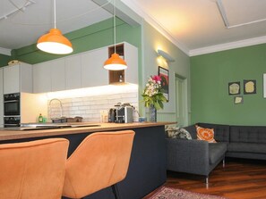 Eine moderne Küche mit Kochinsel, einem Essbereich mit orangefarbenen Stühlen und einem grauen Sofa.